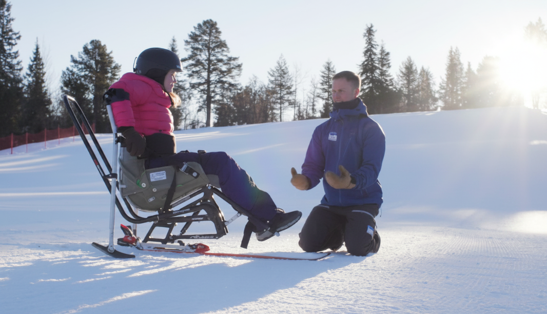Instruktør veileder nybegynner på sit-ski