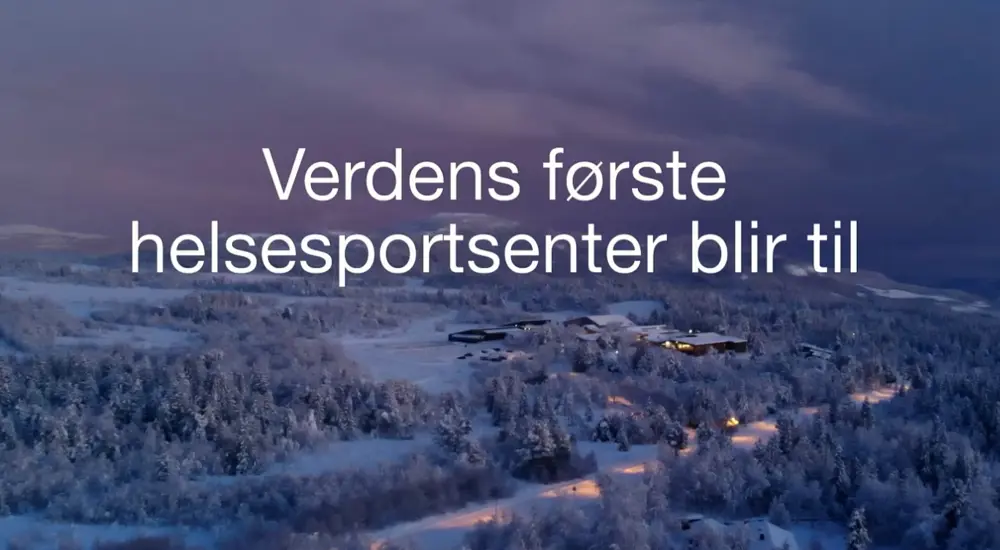 Beitostølen Helsesportsenter sett fra lufta om vinteren, - med teksten "Verdens første helsesportsenter bli til". Foto: Nicolay Flaaten