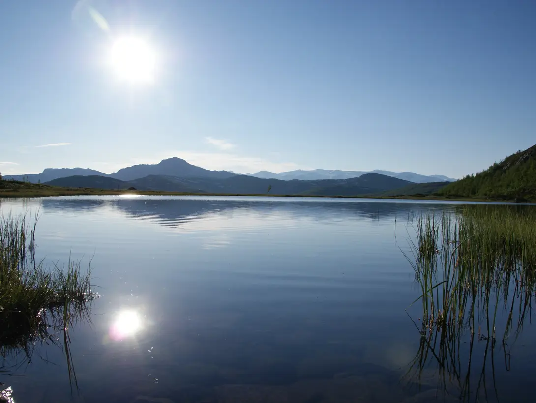 Sola speiler seg i vannet, med fjellet Bitihorn i bakgrunnen