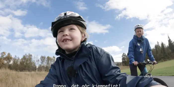 Skjermbilde fra filmen om barne- og ungdomstilbudet ved Beitostølen Helsesportsenter. En jente sykler foran instruktør. 